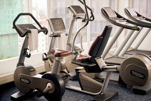 Ein Fitnessraum mit Trainingsgeräten, ein Fenster mit Blick auf Gebäude und ein Teppichboden.