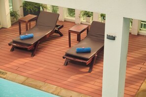 A poolside area with two lounge chairs and a table, wooden deck flooring, and potted plants. - Phnom Penh Katari Hotel (Phnom Penh)