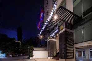 Entrada de hotel con una bandera, una escalera y fachada de edificio moderno.