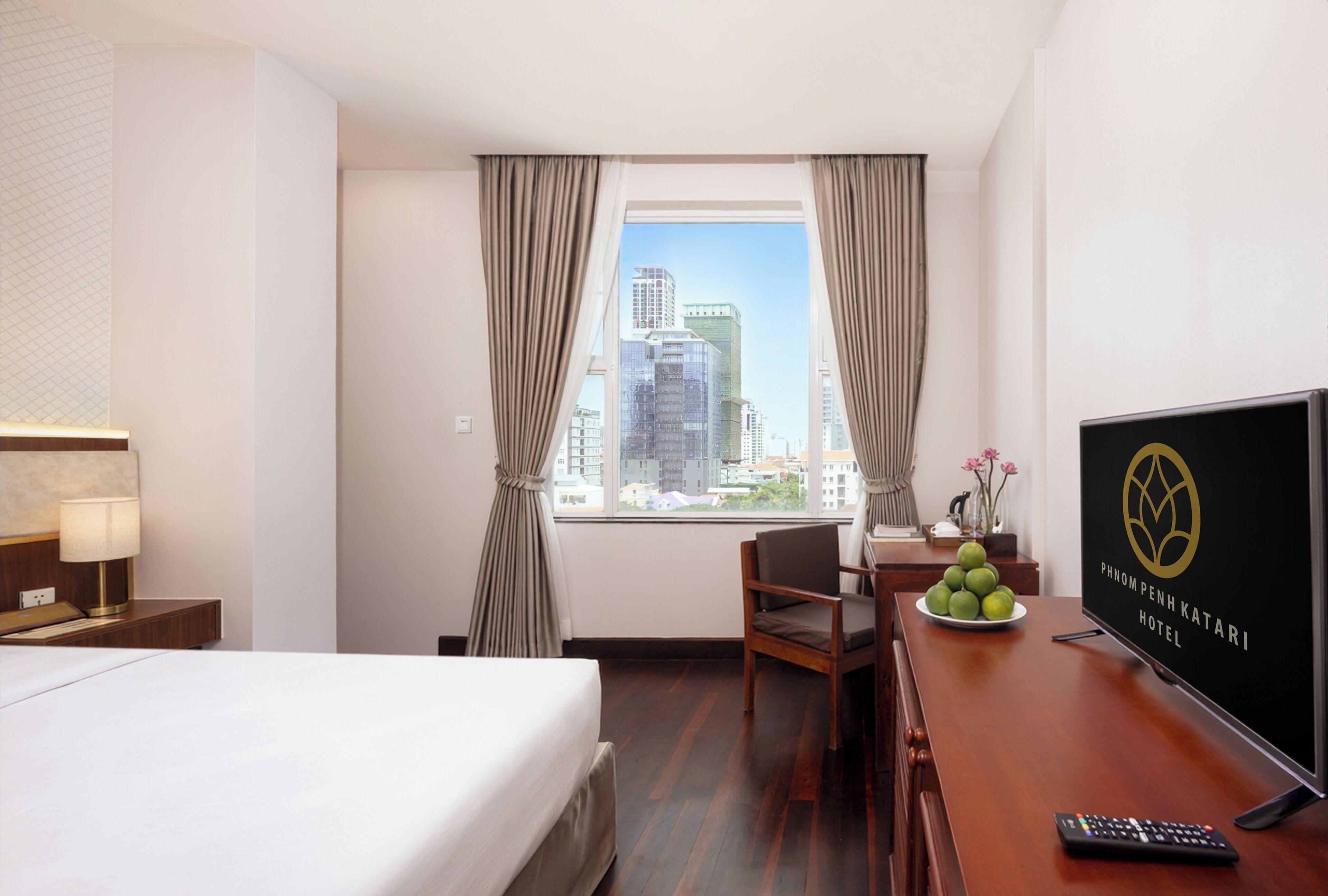 Habitación de hotel con cama, escritorio con una fuente de frutas, control remoto y ventana con cortinas.