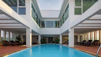 Piscina interior moderna con una escalera central y zonas de descanso a cada lado.