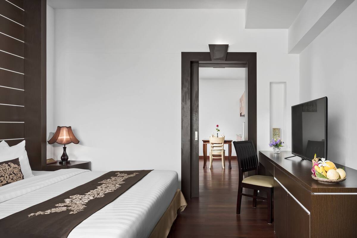 Une chambre d’hôtel avec un lit, un bureau avec une télévision, une chaise et une petite table avec des fruits.