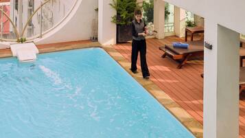 Une zone autour d’une piscine, avec une personne tenant un plateau, une chaise longue et une petite table.
