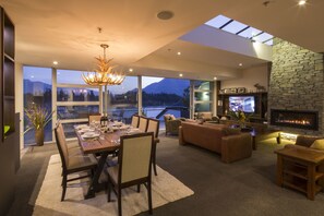 A modern living room with a fireplace, a dining area, and large windows offering a view of mountains and a lake.
