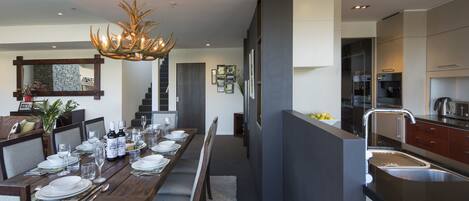A modern kitchen with a dining area, featuring a wooden table set for six, a chandelier, and a built-in island with a sink.