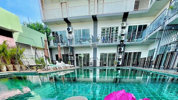 A breakfast setting with toast, eggs, and ham on a wooden table by a poolside, with a view of a modern building and a clear blue pool. - Anantra Resort Pattaya (Pattaya)