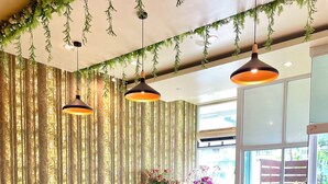 A dining area with round tables and cushioned chairs, a wooden floor, and a view of the outdoors through large windows. - Anantra Resort Pattaya (Pattaya)