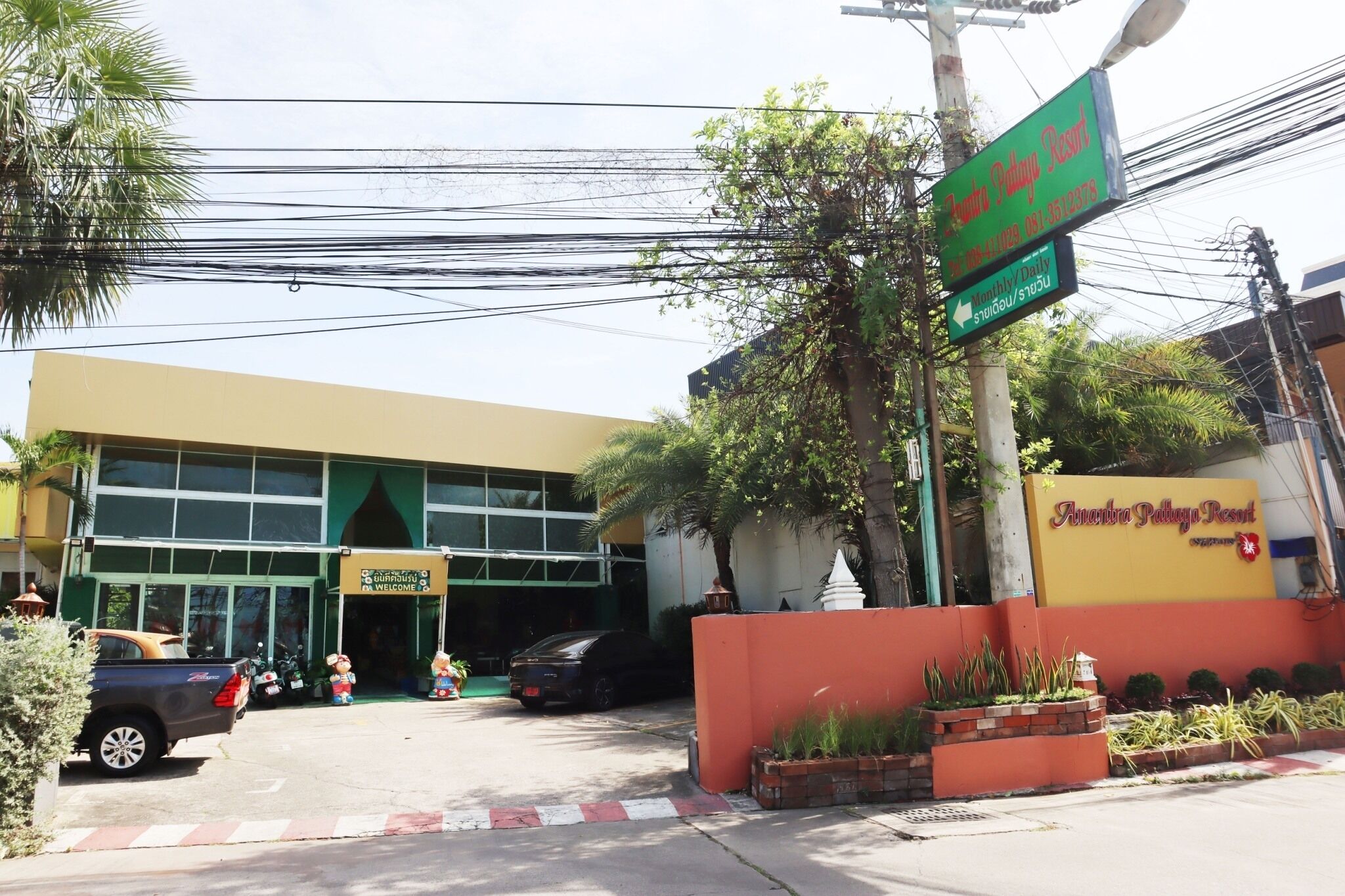 A building with a sign for Anjana Palaya Resort, a gated entrance, and parked cars.