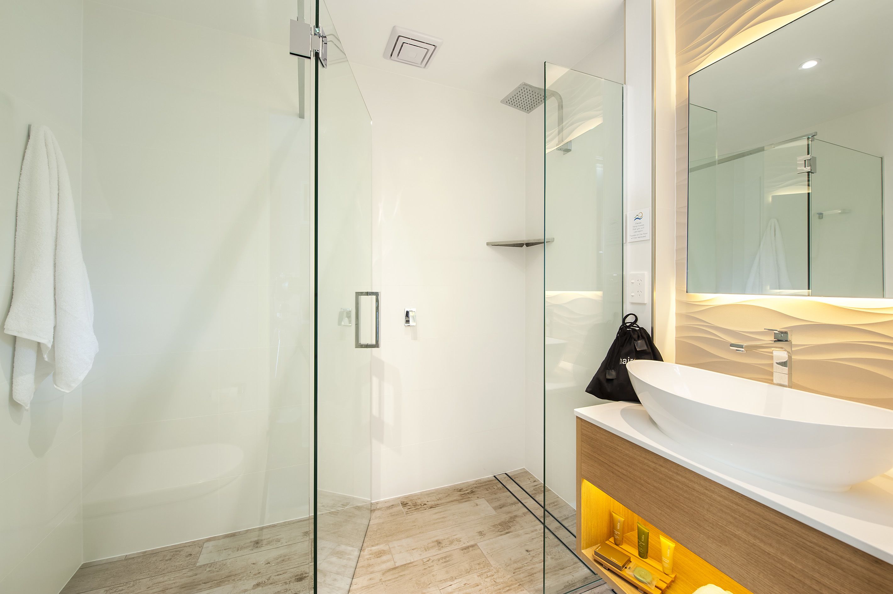 A modern bathroom with a glass-enclosed shower, a large mirror, and a wooden vanity with a white sink.