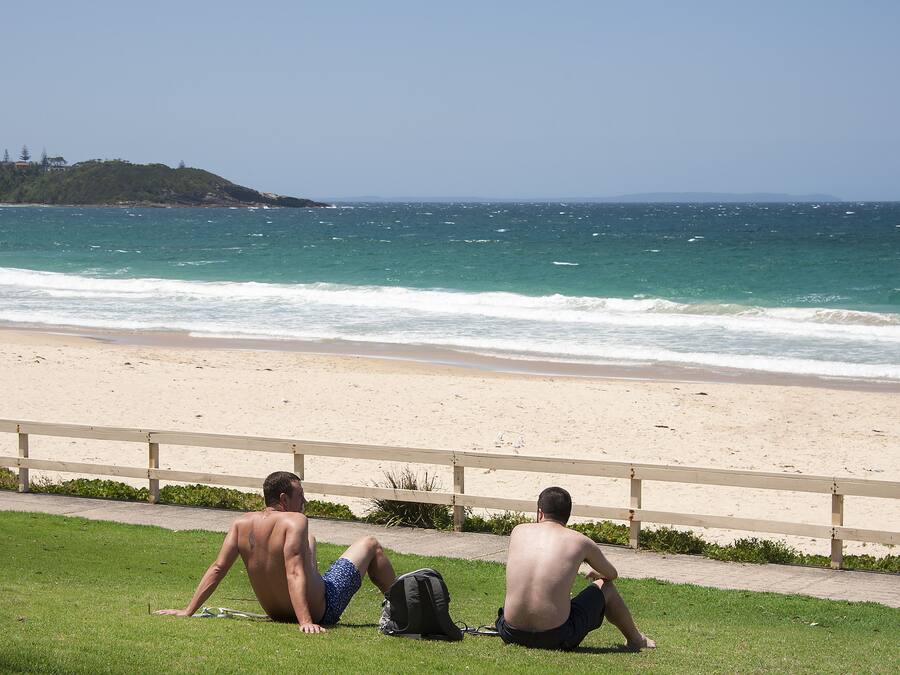 Two men sitting on a grassy area by a beach, overlooking the ocean.