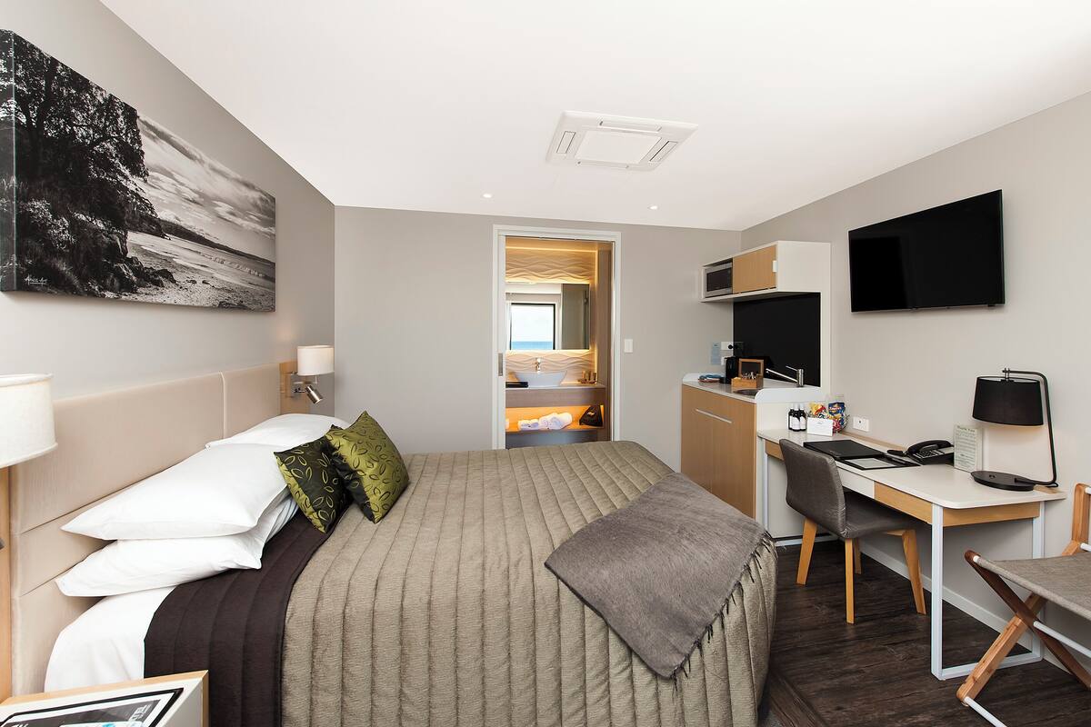 A hotel room with a bed, desk, and kitchenette.