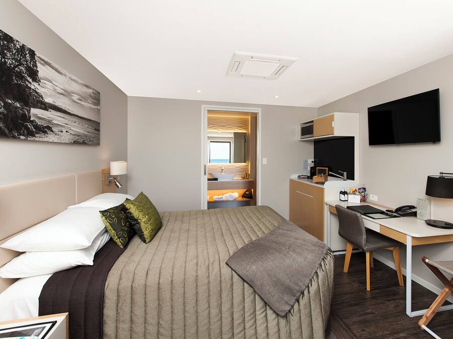 A hotel room with a bed, desk, and kitchenette.
