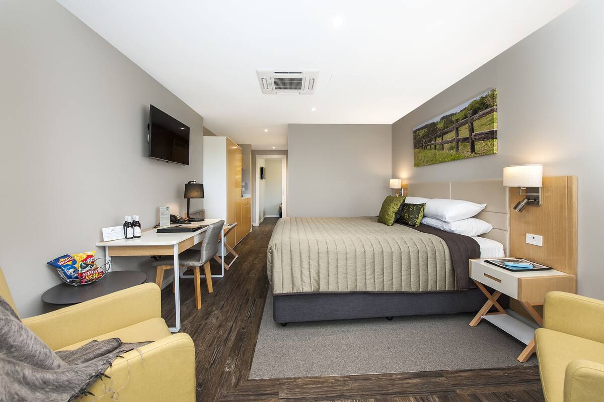 A modern hotel room with a bed, desk, chair, and a TV mounted on the wall.