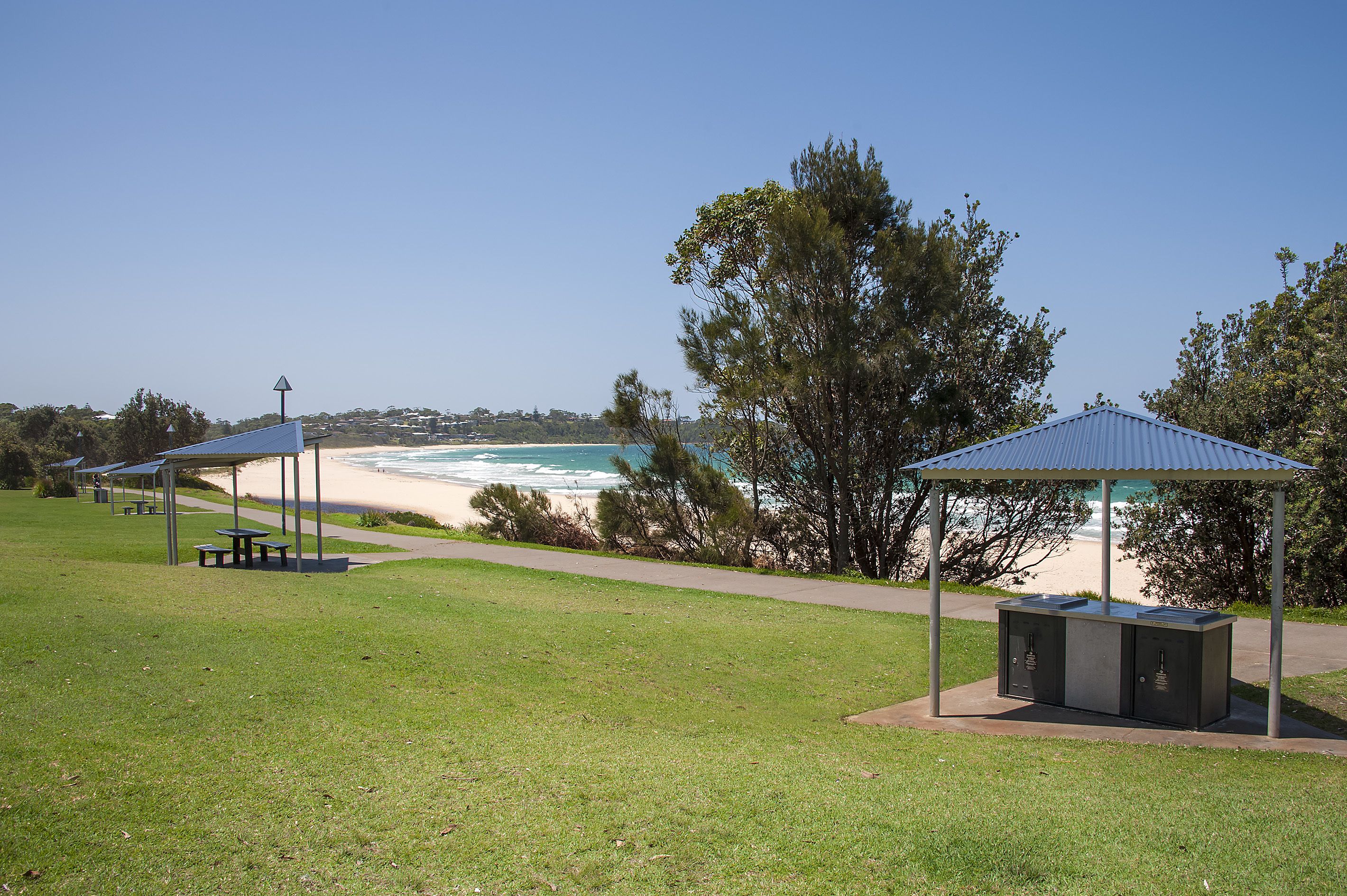 A beachside park with picnic tables and a barbecue area.