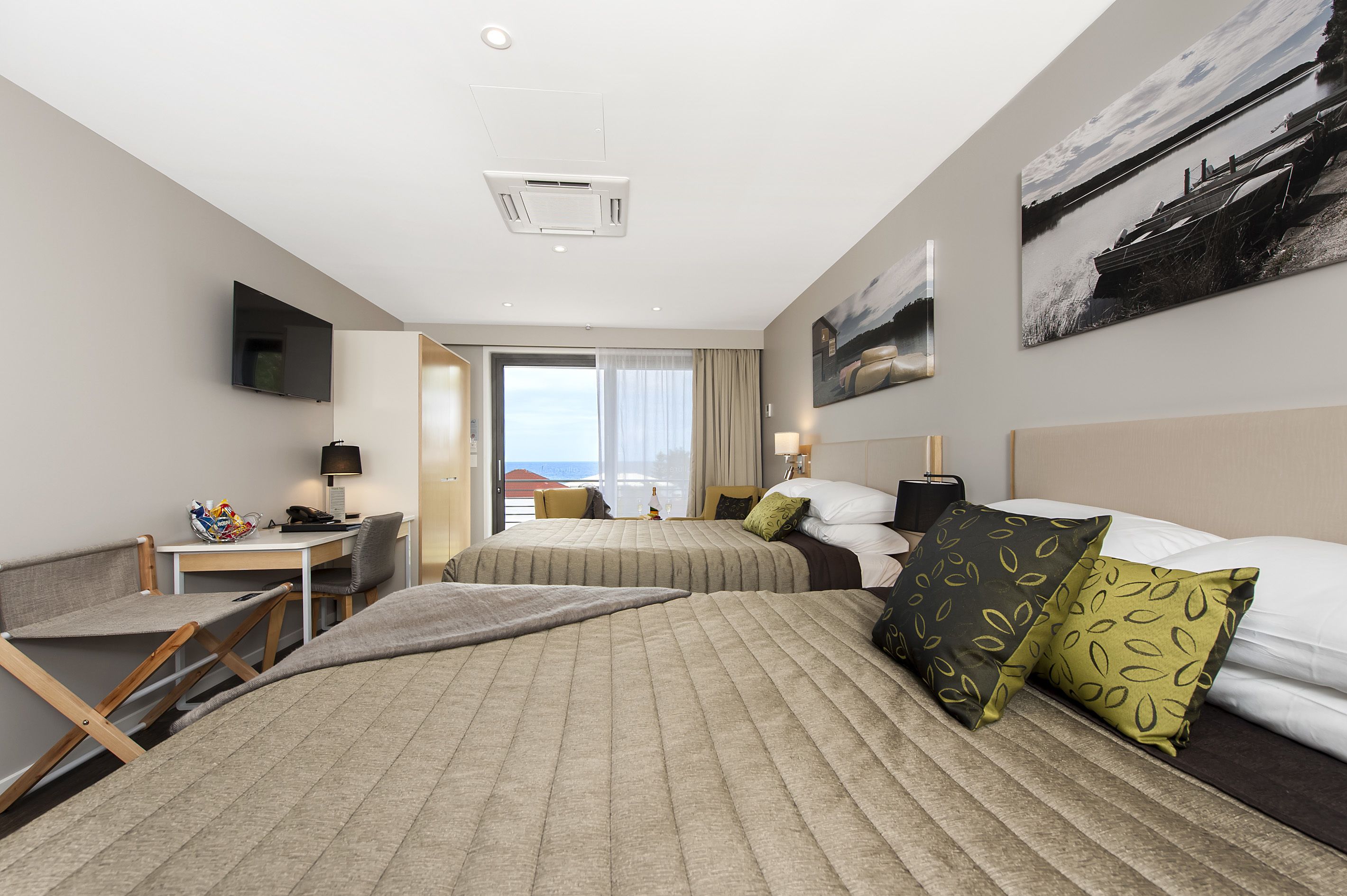 Une chambre d’hôtel avec deux lits, un bureau, une chaise, une télévision et une grande fenêtre donnant sur la mer.