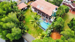 Vista aérea de um resort com piscina, vegetação exuberante e um corpo d'água.