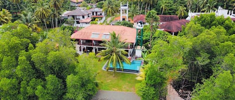 A tropical resort with a swimming pool, surrounded by lush greenery and palm trees.