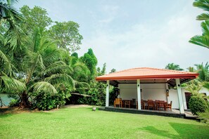 A covered outdoor seating area with a red roof, surrounded by lush greenery and palm trees. - Lagoon Bentota (Bentota)