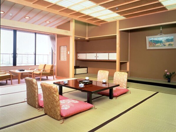 A traditional Japanese-style room with tatami flooring, a low table with cushions, and a view of a garden through large windows.