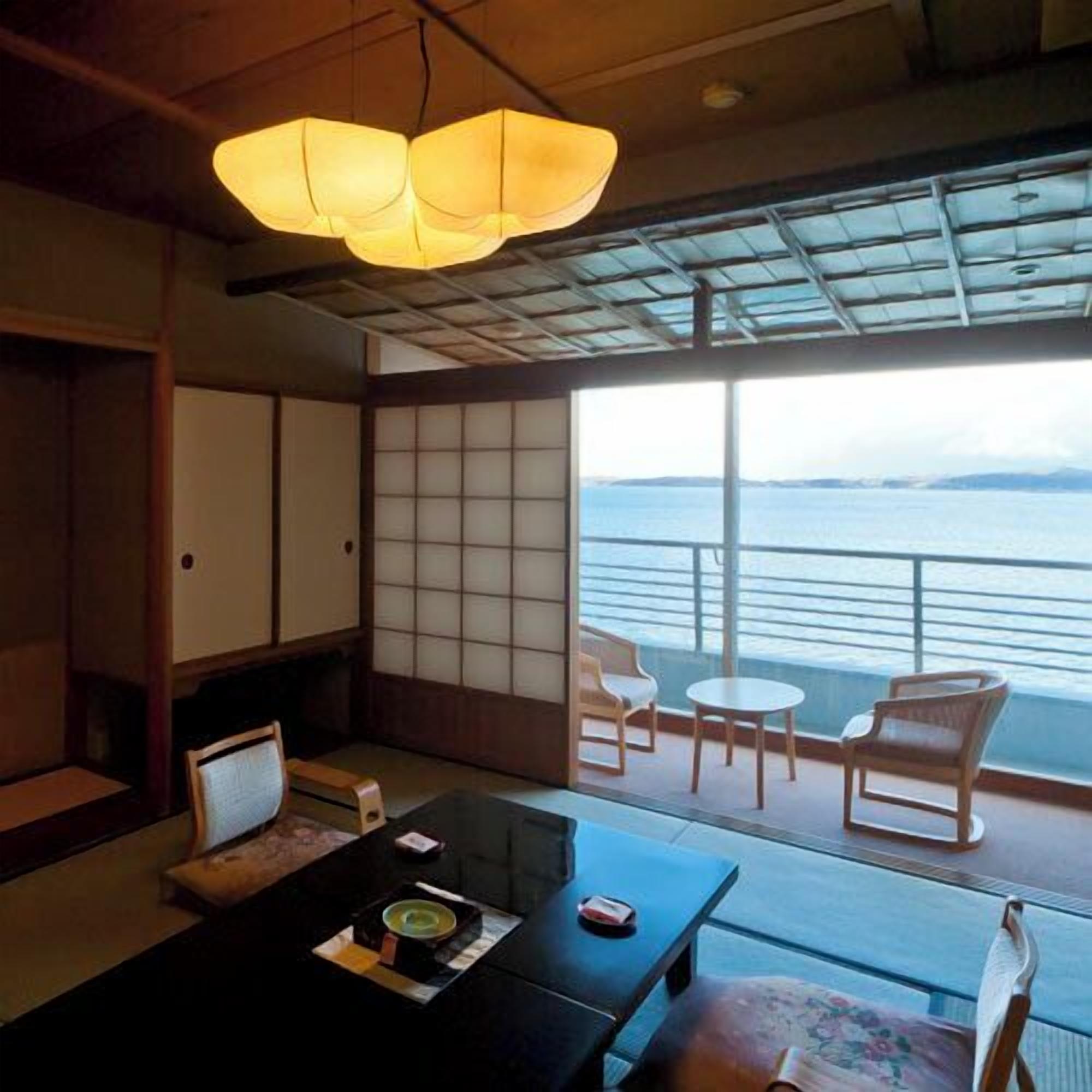 Une pièce de style japonais traditionnel, avec un sol recouvert de tatamis, une petite table sur laquelle est disposé un service à thé, et une vue sur la mer grâce à de grandes portes coulissantes.