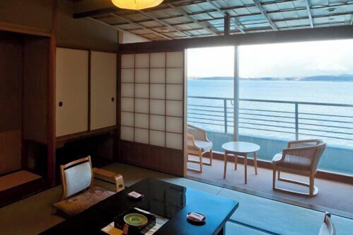 Une pièce de style japonais traditionnel, avec un sol recouvert de tatamis, une petite table sur laquelle est disposé un service à thé, et une vue sur la mer grâce à de grandes portes coulissantes.