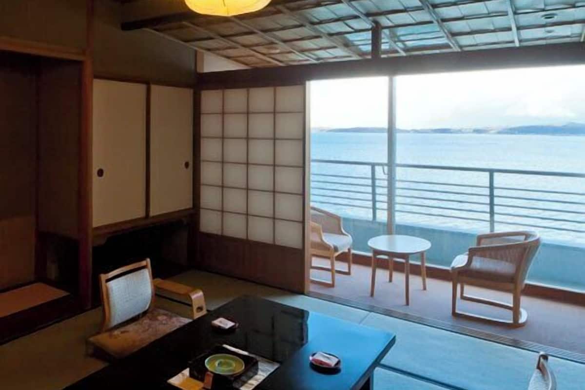 A traditional Japanese room with tatami flooring, a low table with a tea set, and a view of the sea through large sliding doors.