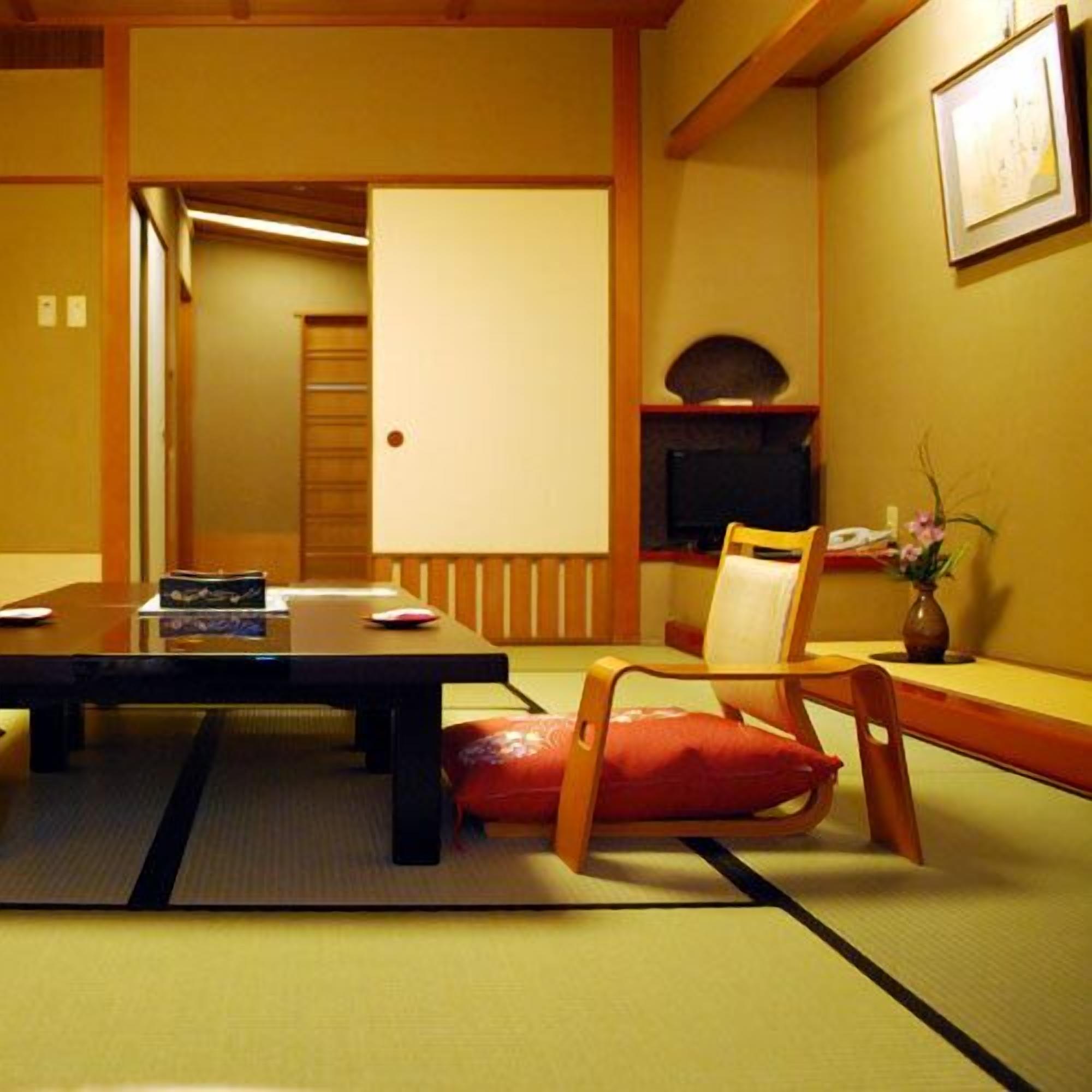 Une pièce de style japonais traditionnel, avec un sol recouvert de tatamis, une table basse, un téléviseur et une petite étagère sur laquelle est posé un vase.