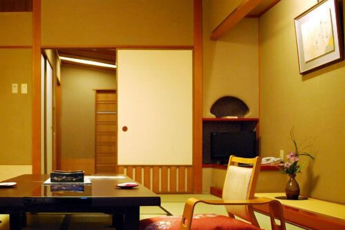 Une pièce de style japonais traditionnel, avec un sol recouvert de tatamis, une table basse, un téléviseur et une petite étagère sur laquelle est posé un vase.