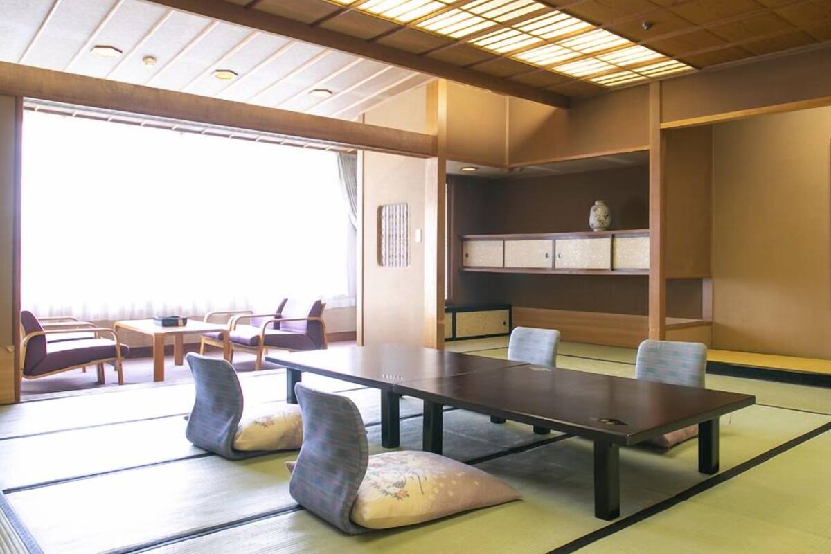 A traditional tatami mat room with a low table, chairs, and a shelf with decorative items.