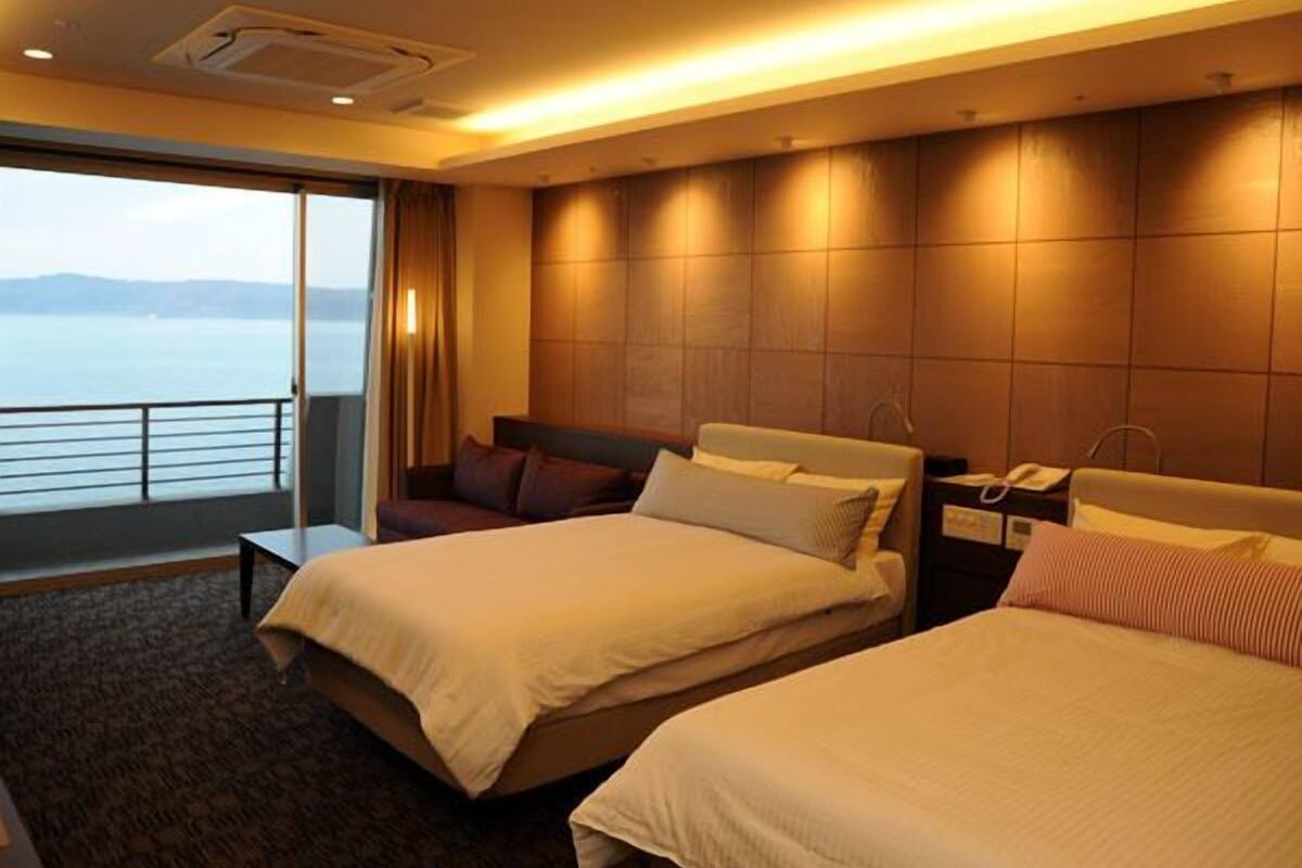 Une chambre d’hôtel avec deux lits, une grande fenêtre donnant sur la mer, une table de chevet avec un téléphone et un climatiseur fixé au mur.