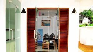 Entrada de hotel con puerta de cristal, contraventanas de madera, un ventilador de techo y un cuadro en la pared.