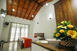 Un dormitorio con techo de madera, una cama, un escritorio y un florero con flores.