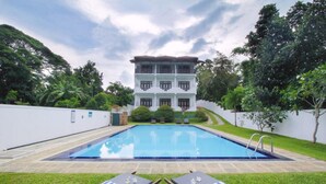 Una piscina con dos sillas de descanso, rodeada de un césped cuidado y un edificio con varios balcones al fondo.