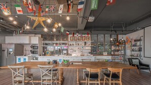 A modern kitchen with a wooden table, chairs, and a variety of flags hanging from the ceiling. - Light Hostel (Tainan)