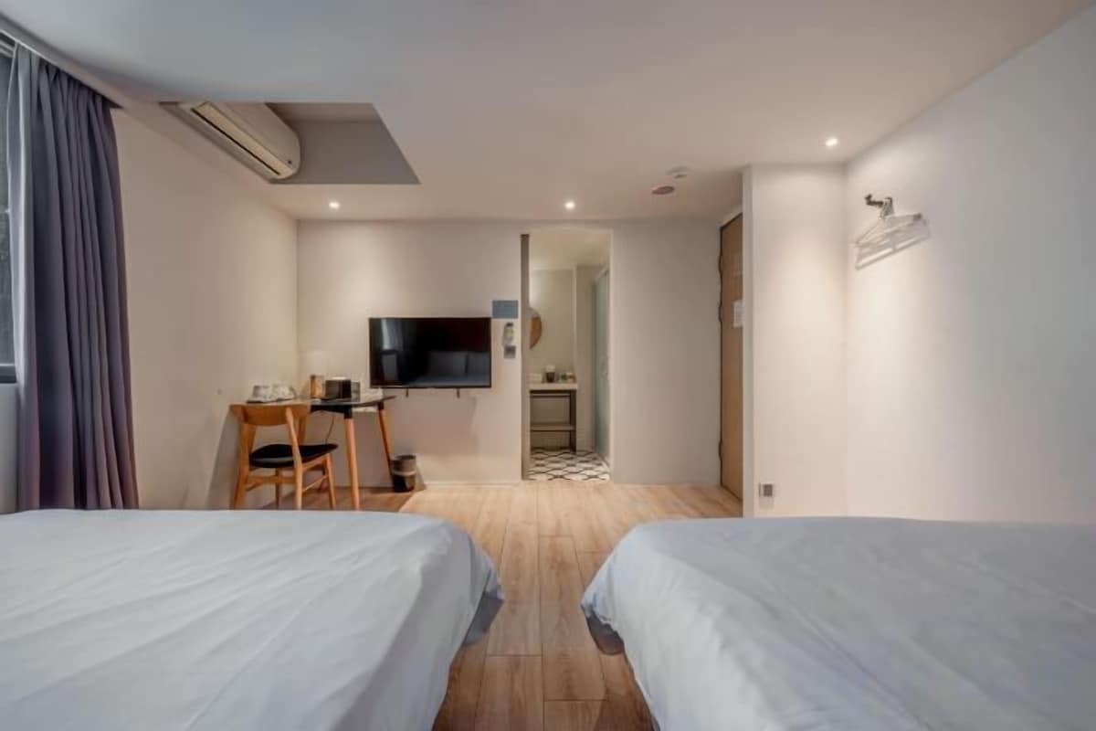 A hotel room with two beds, a desk with a chair, a television, and a small kitchenette.