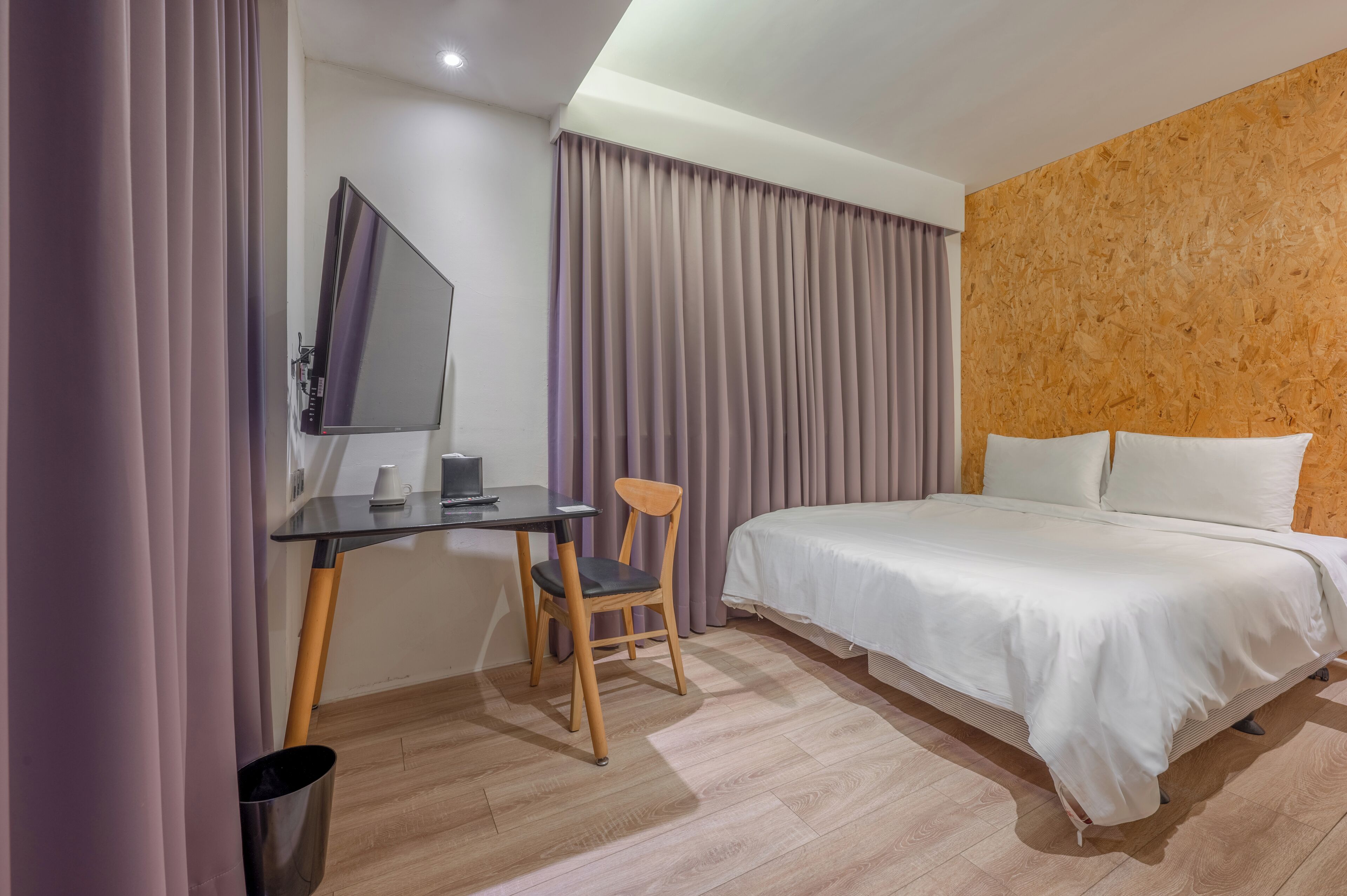 Una habitación de hotel con una cama, un escritorio con una silla, un televisor y cortinas.