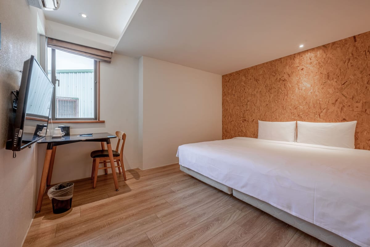 Quarto com cama, escrivaninha com computador, cadeira e janela.