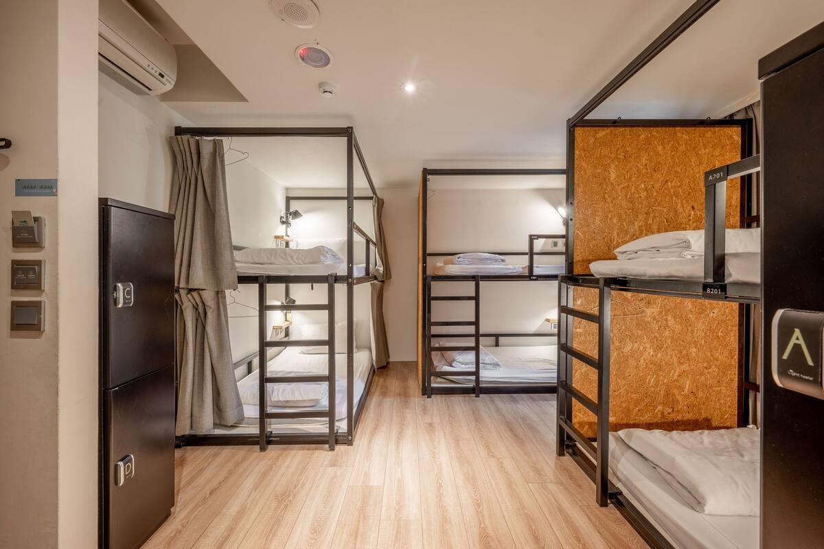 Quarto de hotel compacto com beliches, guarda-roupa e pequena cozinha equipada.