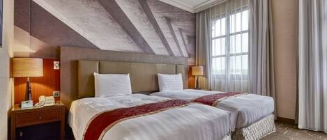 A hotel room with two beds, a large window with curtains, a wooden headboard, and a textured ceiling.