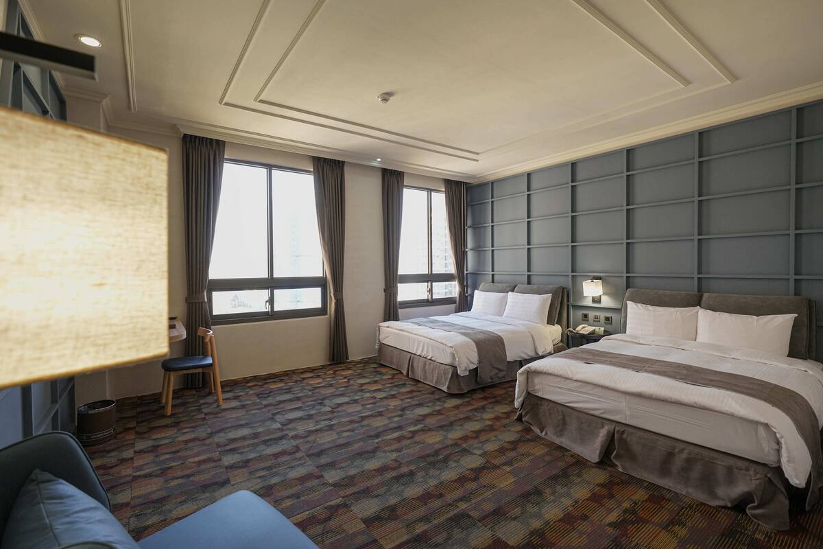 Ein Hotelzimmer mit zwei Betten, einem Schlafsofa, einem Schreibtisch und einem großen Fenster.