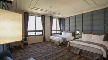 Habitación de hotel con dos camas, un sofá, un escritorio y un ventanal grande.