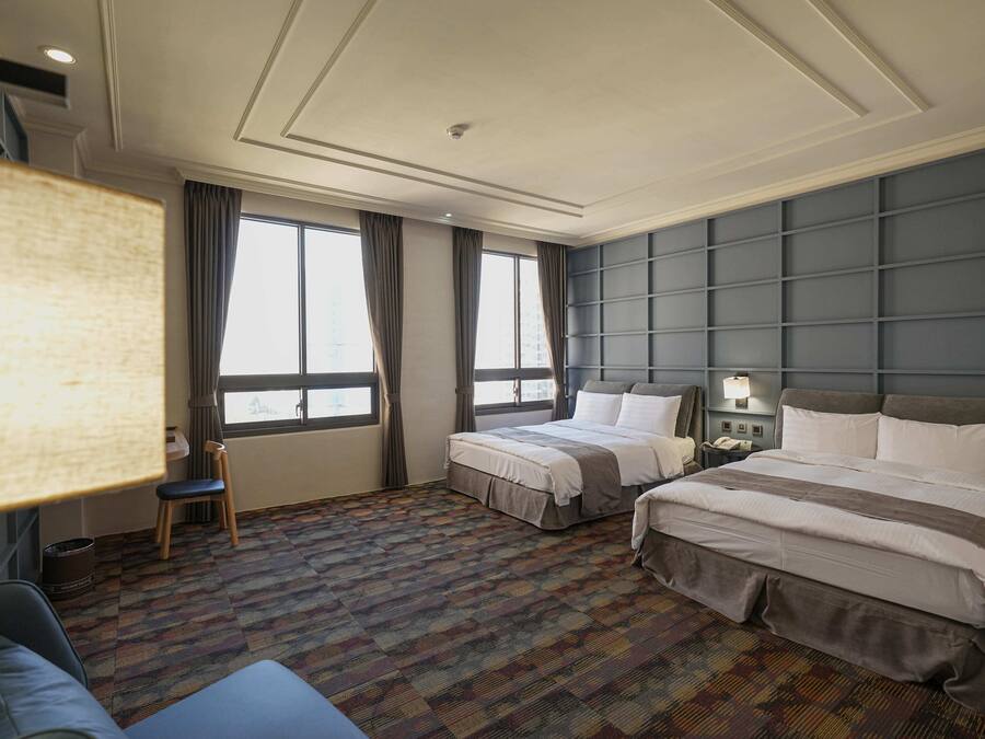 Habitación de hotel con dos camas, un sofá, un escritorio y un ventanal grande.