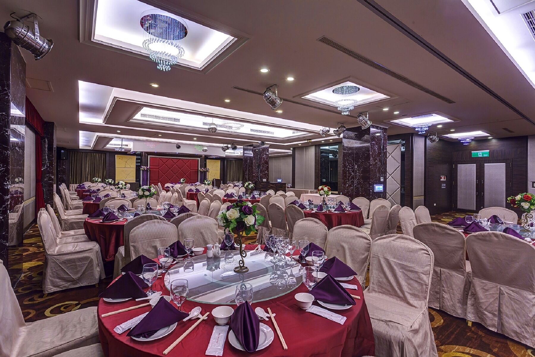 A banquet hall with round tables, chairs, and chandeliers.