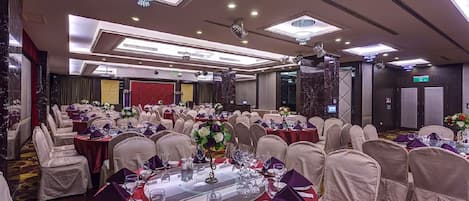A banquet hall with round tables, chairs, and chandeliers.