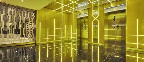 Un ascensor moderno con piso reflectante y patrones de luz geométricos en las paredes.