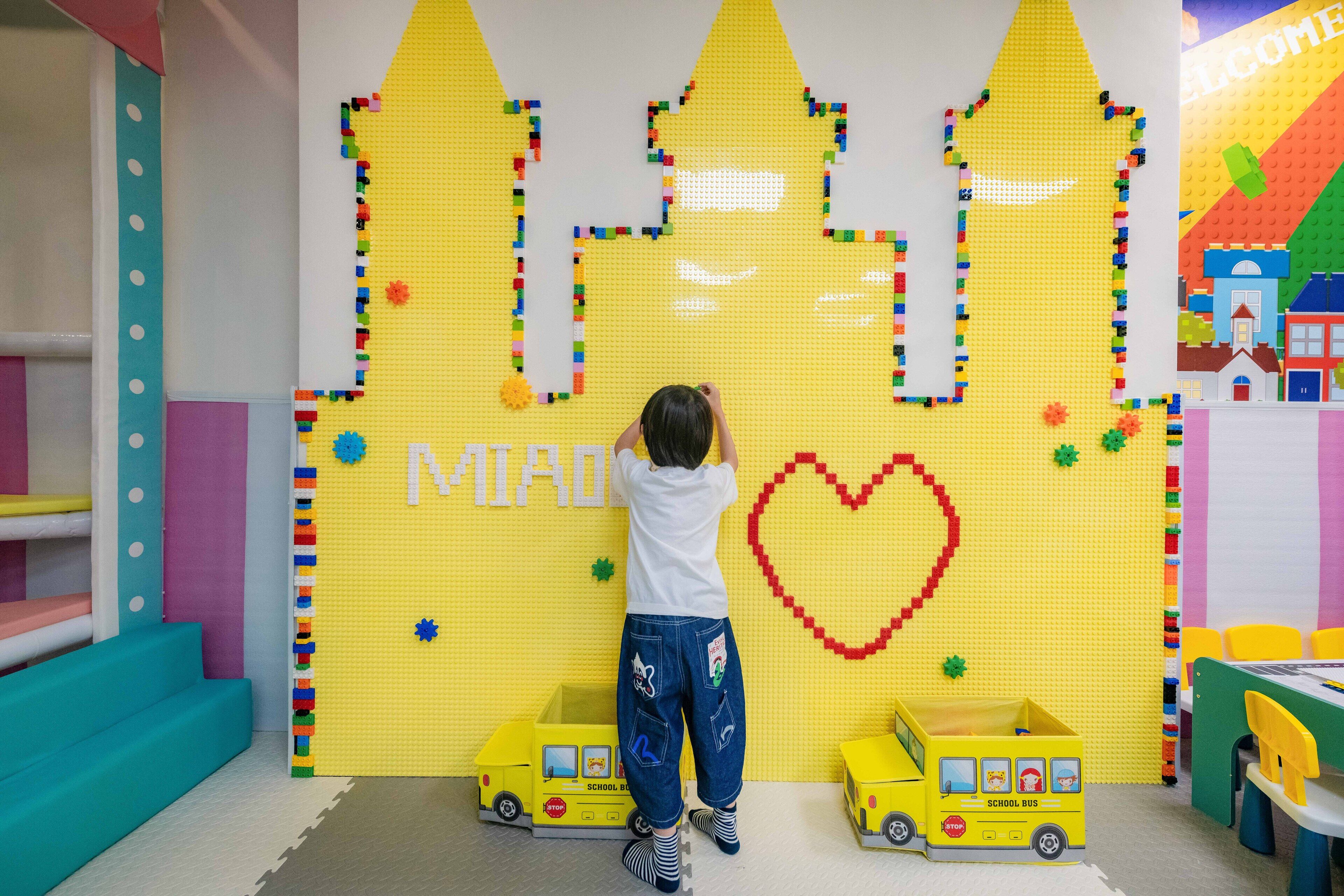 A child playing with LEGO bricks on a wall, with two toy school buses in front.