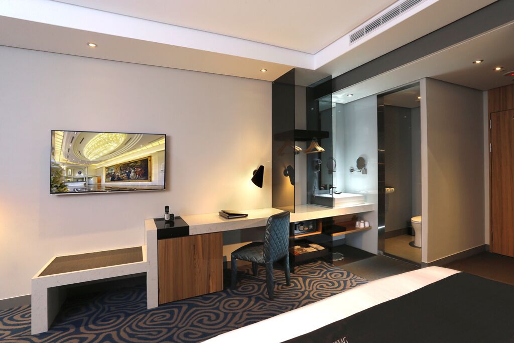A modern hotel room with a large mirror, a desk, a chair, and a bathroom visible through an open door.