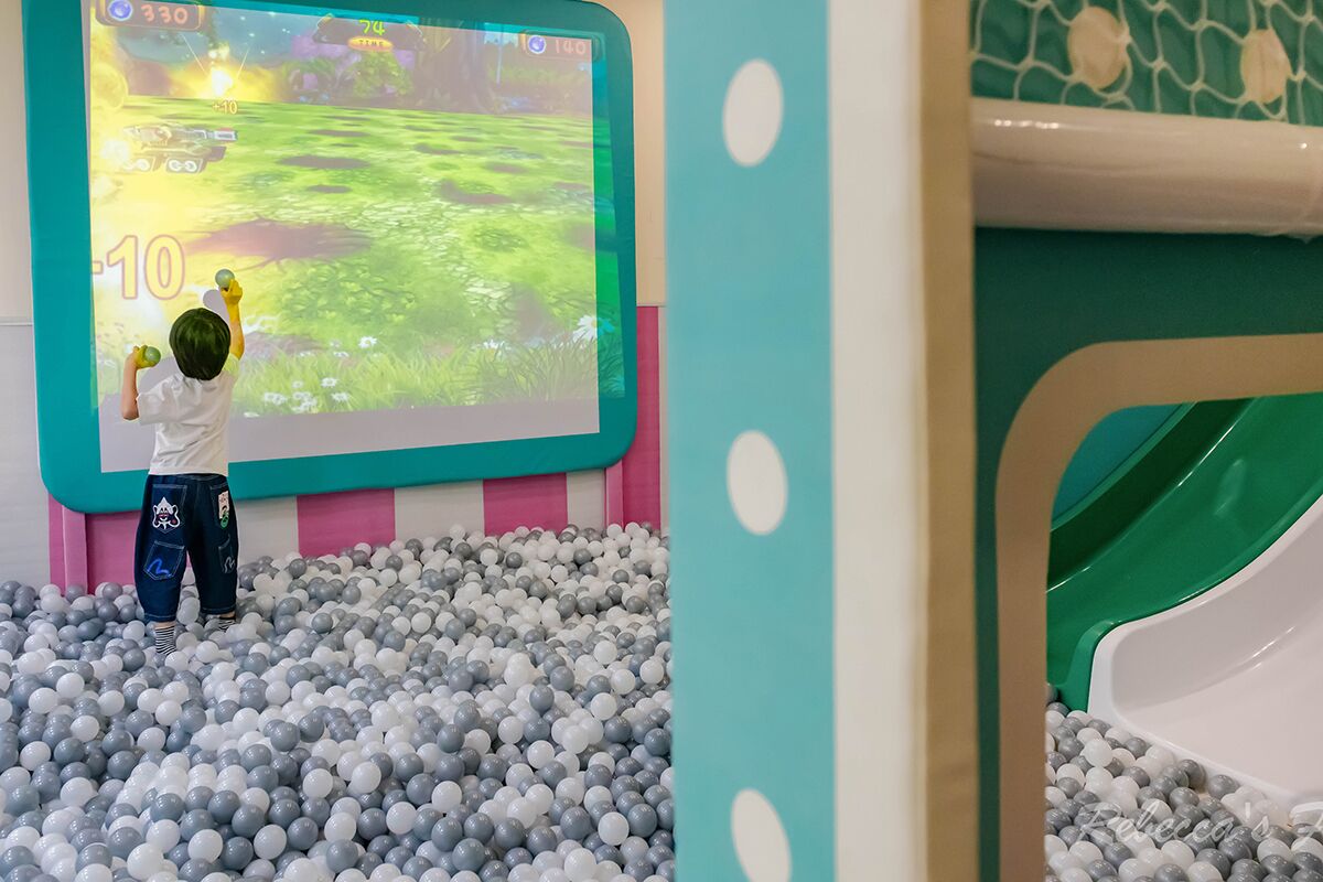 A child playing in a ball pit with a projected game on the wall.