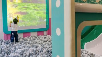A child playing in a ball pit with a projected game on the wall.