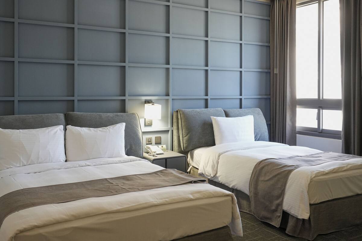 Ein Hotelzimmer mit zwei Betten, einem Nachttisch, einer Lampe und einem Fenster mit Vorhängen.
